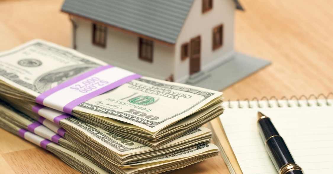 stacks of cash next to a house figurine and a notepad